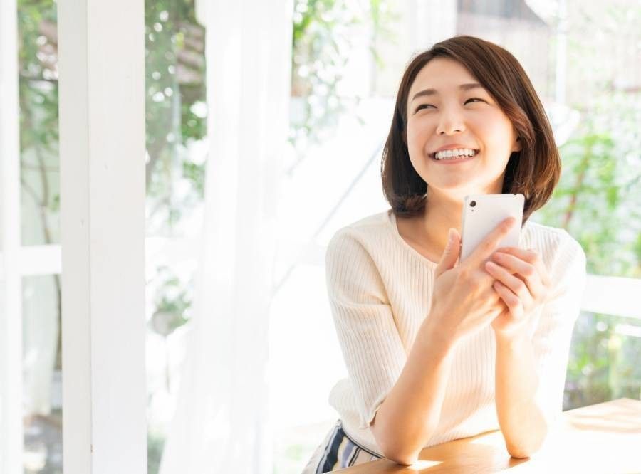 スマホを持って笑顔の女性の画像